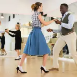 Coppia balla swing in una scuola di ballo. Altri ballerini si esercitano nello specchio.