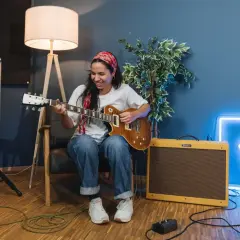 Donna sorridente suona la chitarra, con un'insegna al neon blu sullo sfondo che ricorda le "blue canzoni famose".