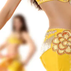 Dettaglio di una ballerina che esegue una danza del ventre, con abito giallo decorato e velo colorato.