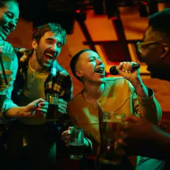 Amici che cantano a squarciagola, bevendo e divertendosi con duetti karaoke facili in un locale illuminato da luci colorate.