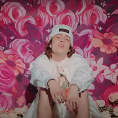Sangiovanni in Malibù, seduto su un letto di rose, con uno sfondo floreale vibrante.