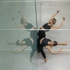 Due ballerine in abiti neri eseguono movimenti fluidi, riflesse su una parete specchiata. Un'immagine che evoca la grazia dei corsi di danza moderna.
