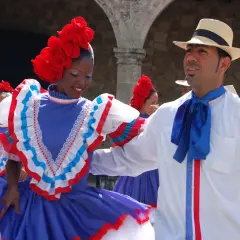 Coppia in abiti tradizionali, lei con fiori rossi sui capelli e un vestito blu con balze, lui con cappello di paglia e fiocco blu, pronti per un vivace ballo di salsa e merengue.