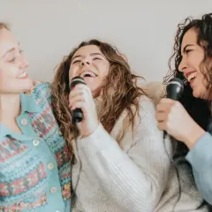 Tre amiche ridono e cantano con microfoni, un momento di gioia con canzoni facili da cantare.