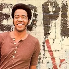 Bill Withers sorride davanti a un muro con graffiti. Anche se "ain't no sunshine", il suo sorriso illumina la scena.