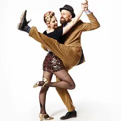 A man in a tan suit dips a woman in a sequined skirt during a Lindy Hop dance.