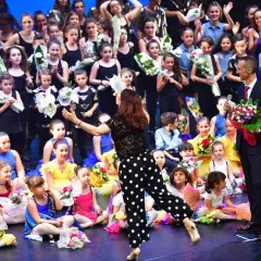 Giovani ballerini festeggiano sul palco dopo un'esibizione di rumba ballo latino americano, ricevendo fiori e applausi.