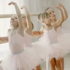 Bambine in tutù rosa praticano la danza propedeutica alla sbarra, con braccia alzate e sguardi concentrati.