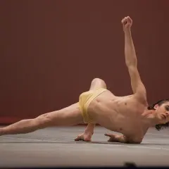 Un ballerino esegue un complesso floor work, con un braccio teso verso l'alto e una gamba distesa.
