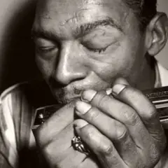 L'uomo con l'armonica chiude gli occhi, immerso nella melodia blues che esce dallo strumento.