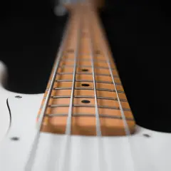 Primo piano del manico di un basso elettrico bianco, con le corde metalliche che corrono lungo la tastiera in legno chiaro.