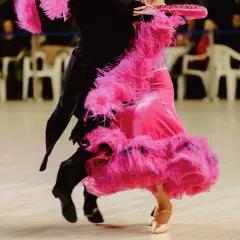 Coppia di ballerini in un vivace fox trot. La donna indossa un abito rosa con piume, l'uomo un completo nero.