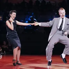 Coppia in abito elegante e vestito scuro si diverte in un energico ballo boogie woogie sul palco di un festival.