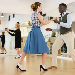Coppia balla swing in una scuola di ballo. Altri ballerini si esercitano nello specchio.