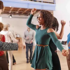 Persone di varie età si divertono con balli caraibici singoli in una sala luminosa, con sorrisi e movimenti energici.