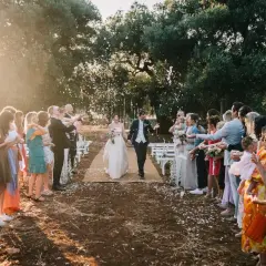 Sposi camminano su un tappeto, circondati da invitati che lanciano petali. La luce del tramonto crea un'atmosfera magica, perfetta per una canzone matrimonio.