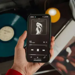 Mano che tiene uno smartphone con la copertina di un album di Taylor Swift. Accanto, un vinile blu e la copertina di "Midnights". Nonostante l'atmosfera moderna, si percepisce il fascino delle canzoni sudamericane.