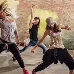 Un gruppo di ballerini energici in un ambiente urbano, circondati da fumo giallo. Un esempio di video dance cos'è: pura espressione e movimento.