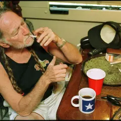 Willie Nelson, icona delle migliori canzoni country americane, accende una sigaretta con una tazza di caffè accanto.