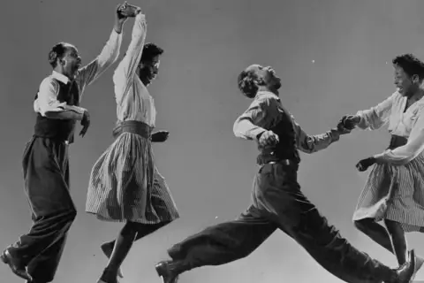 Coppia balla il lindy hop con energia e gioia, in un'esplosione di movimento e ritmo.