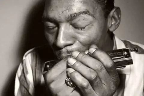 L'uomo con l'armonica chiude gli occhi, immerso nella melodia blues che esce dallo strumento.