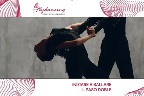Two dancers in black outfits perform a dramatic Paso Doble pose against a grey backdrop.