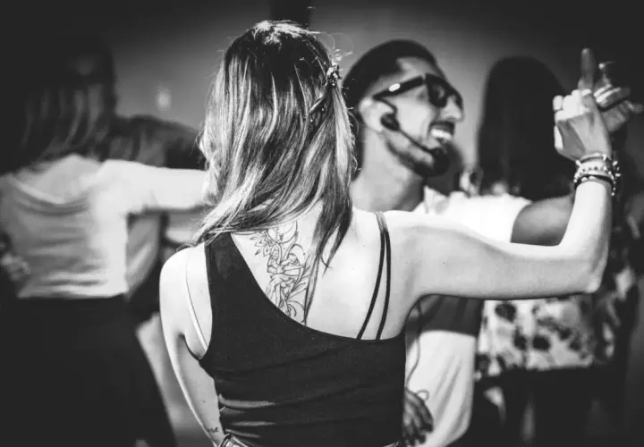 Coppie danzano in un corso di ballo latino americano. La donna in primo piano ha un tatuaggio sulla schiena.