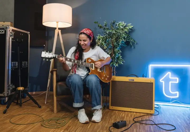 Donna sorridente suona la chitarra, con un'insegna al neon blu sullo sfondo che ricorda le "blue canzoni famose".