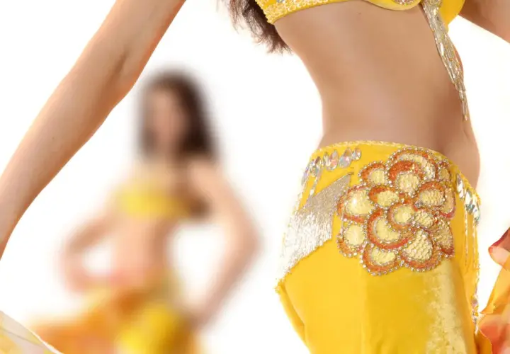 Dettaglio di una ballerina che esegue una danza del ventre, con abito giallo decorato e velo colorato.
