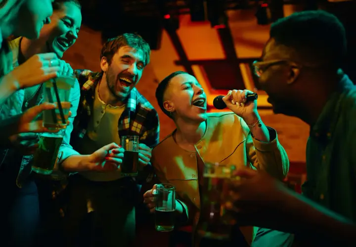 Amici che cantano a squarciagola, bevendo e divertendosi con duetti karaoke facili in un locale illuminato da luci colorate.
