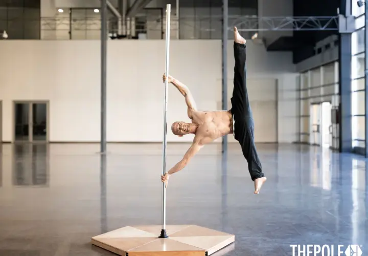 Uomo in posa acrobatica su un palo, dimostra che anche i pole dance principianti possono raggiungere incredibili posizioni con la giusta dedizione.