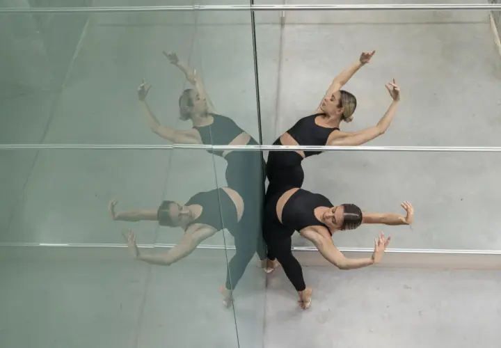 Due ballerine in abiti neri eseguono movimenti fluidi, riflesse su una parete specchiata. Un'immagine che evoca la grazia dei corsi di danza moderna.