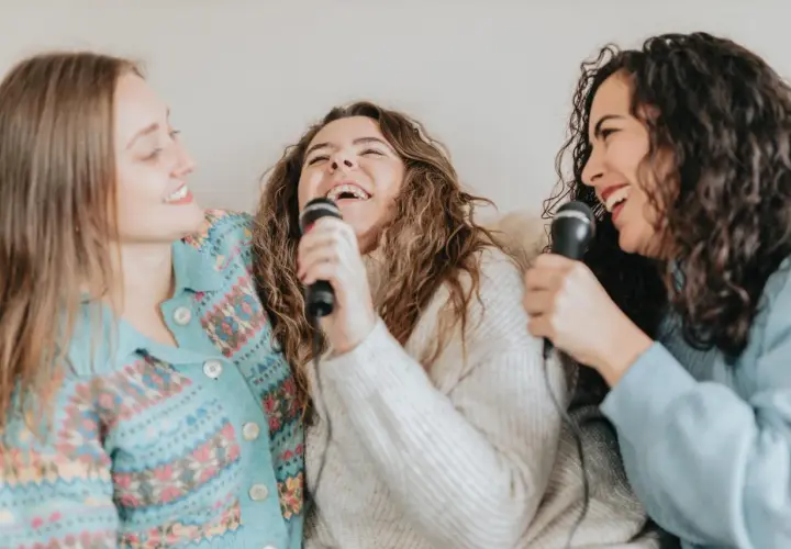 Tre amiche ridono e cantano con microfoni, un momento di gioia con canzoni facili da cantare.