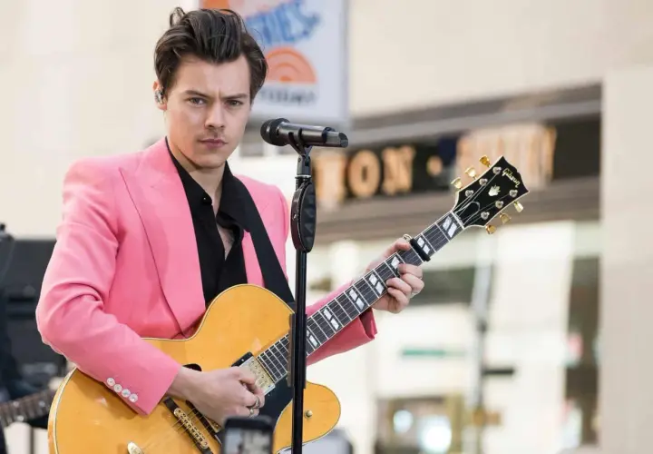 Harry Styles con giacca rosa suona la chitarra, ispirando tante canzoni da suonare con la chitarra.