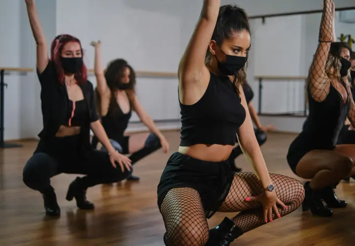 Ragazze in abiti neri e maschere eseguono una energica danza reggaeton in sala prove.