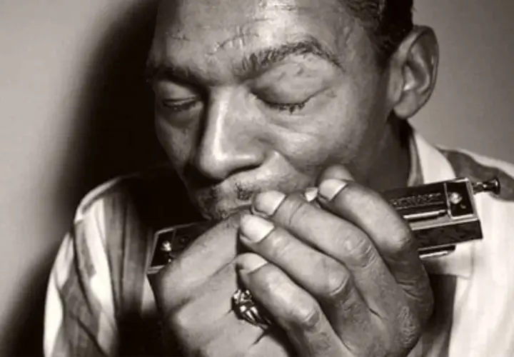 L'uomo con l'armonica chiude gli occhi, immerso nella melodia blues che esce dallo strumento.