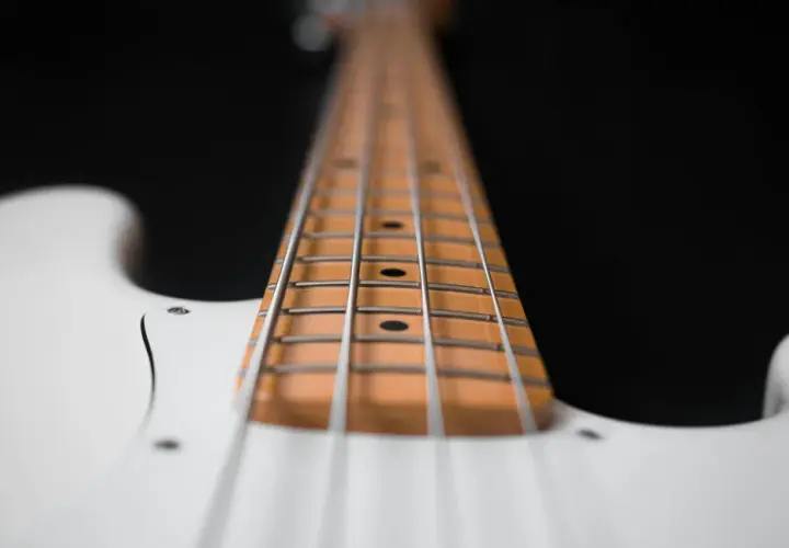 Primo piano del manico di un basso elettrico bianco, con le corde metalliche che corrono lungo la tastiera in legno chiaro.