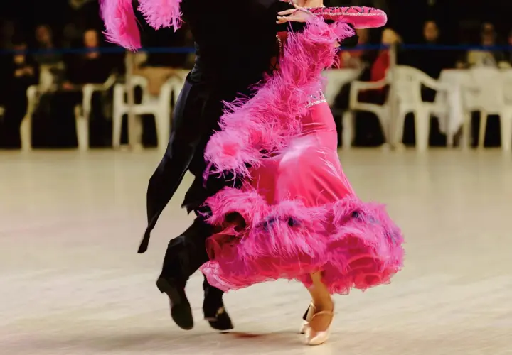 Coppia di ballerini in un vivace fox trot. La donna indossa un abito rosa con piume, l'uomo un completo nero.