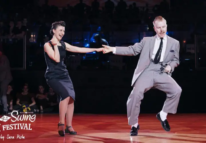 Coppia in abito elegante e vestito scuro si diverte in un energico ballo boogie woogie sul palco di un festival.