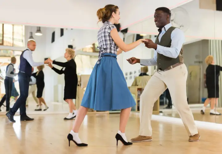 Coppia balla swing in una scuola di ballo. Altri ballerini si esercitano nello specchio.