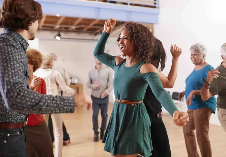 Persone di varie età si divertono con balli caraibici singoli in una sala luminosa, con sorrisi e movimenti energici.