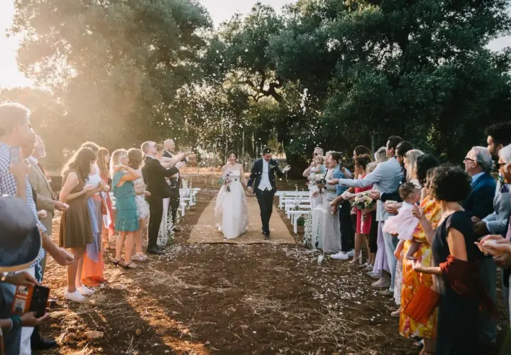 Sposi camminano su un tappeto, circondati da invitati che lanciano petali. La luce del tramonto crea un'atmosfera magica, perfetta per una canzone matrimonio.