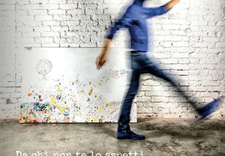 A blurred figure in blue jeans and a jacket walks past a canvas covered in colorful abstract art and doodles.