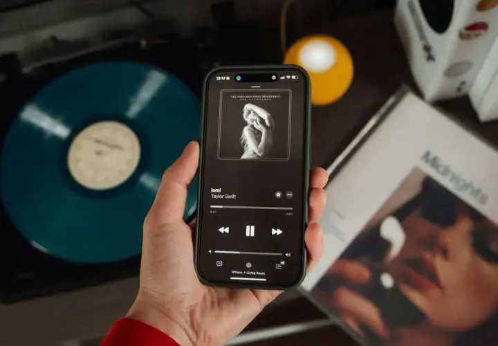 Mano che tiene uno smartphone con la copertina di un album di Taylor Swift. Accanto, un vinile blu e la copertina di "Midnights". Nonostante l'atmosfera moderna, si percepisce il fascino delle canzoni sudamericane.