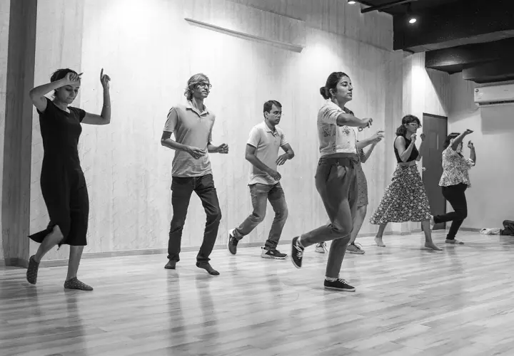 Un gruppo di persone impara come si balla lo swing in una sala prove. Movimenti energici e sorrisi contagiosi.
