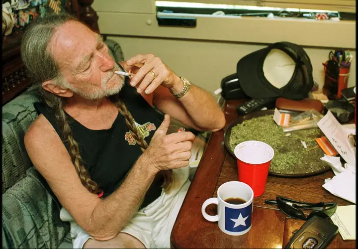 Willie Nelson, icona delle migliori canzoni country americane, accende una sigaretta con una tazza di caffè accanto.