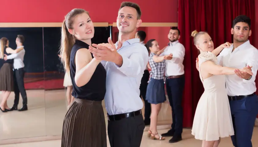 Coppie felici partecipano a corsi di ballo di coppia, imparando passi eleganti in una sala con specchi e tende rosse.
