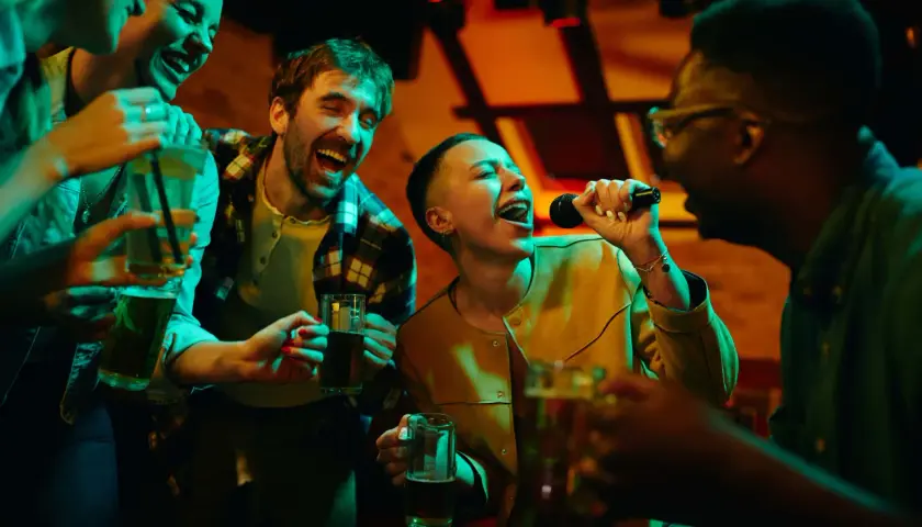 Amici che cantano a squarciagola, bevendo e divertendosi con duetti karaoke facili in un locale illuminato da luci colorate.