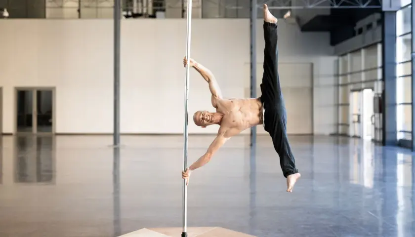 Uomo in posa acrobatica su un palo, dimostra che anche i pole dance principianti possono raggiungere incredibili posizioni con la giusta dedizione.