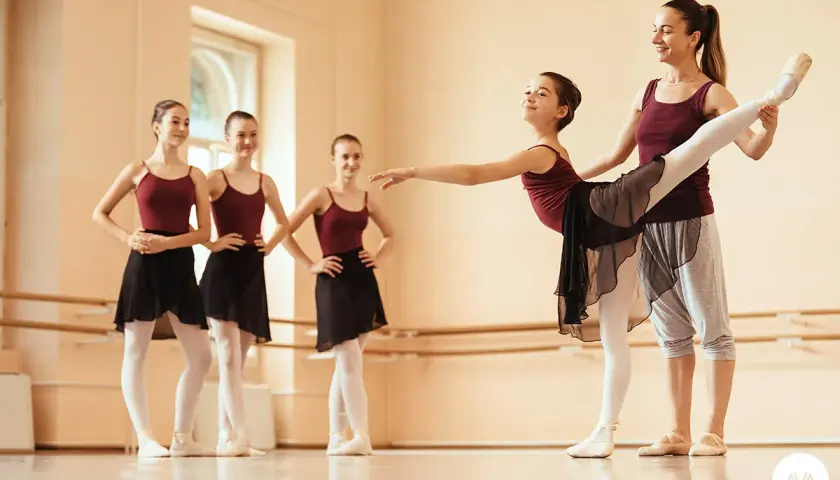 Un'insegnante di danza classica guida una giovane allieva in un esercizio. Altre ballerine attendono il loro turno.